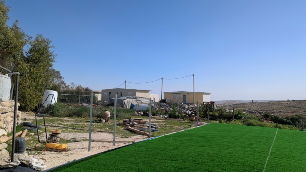 The astroturf at Umm al-Khair, with settler cabins looking on (AI-enhanced image)
